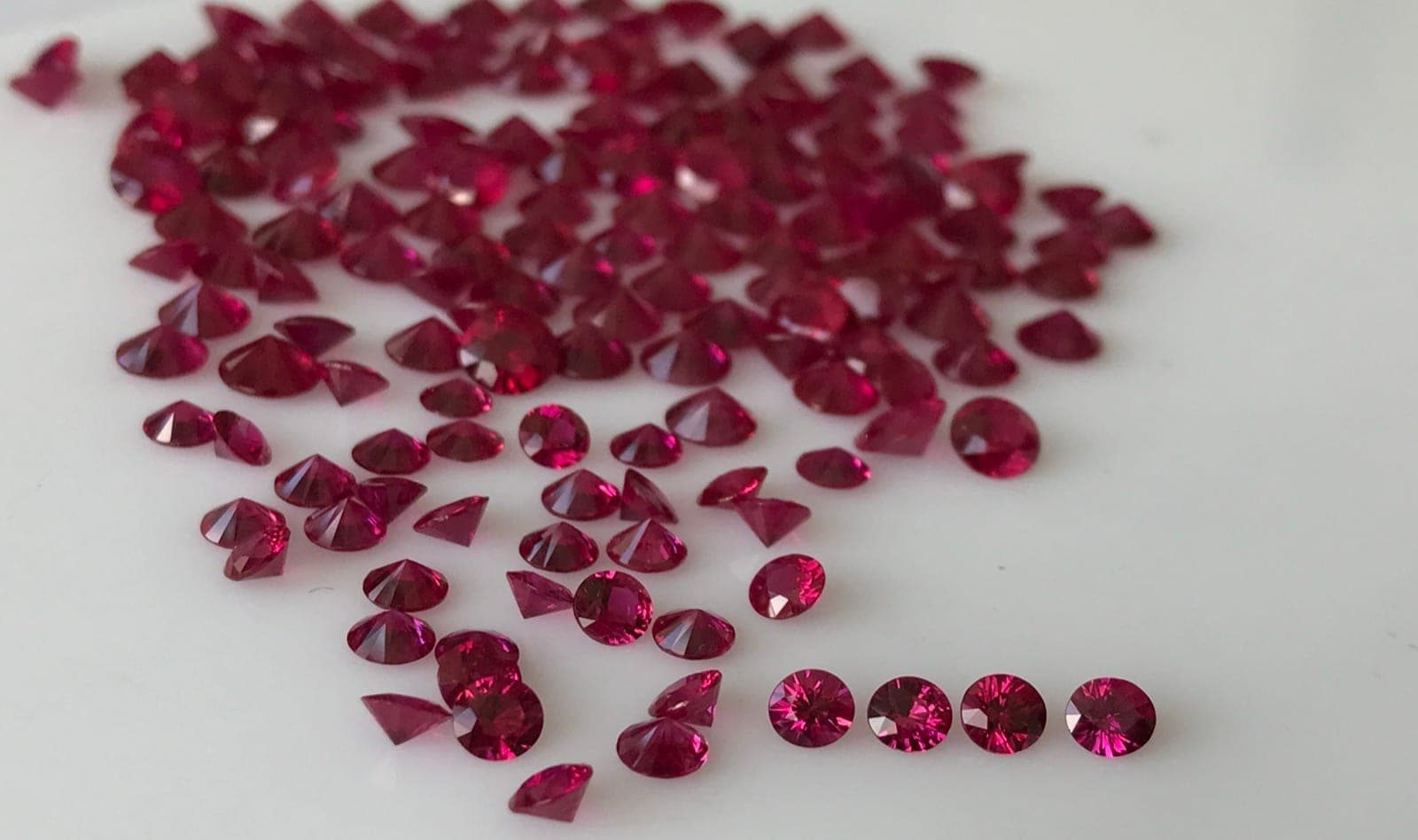Burmese Mogok ruby (left, pure vivid red with strong fluorescence) beside a Mozambique Montepuez ruby (right, vivid red, slightly less fluorescent) under D65 daylight lighting