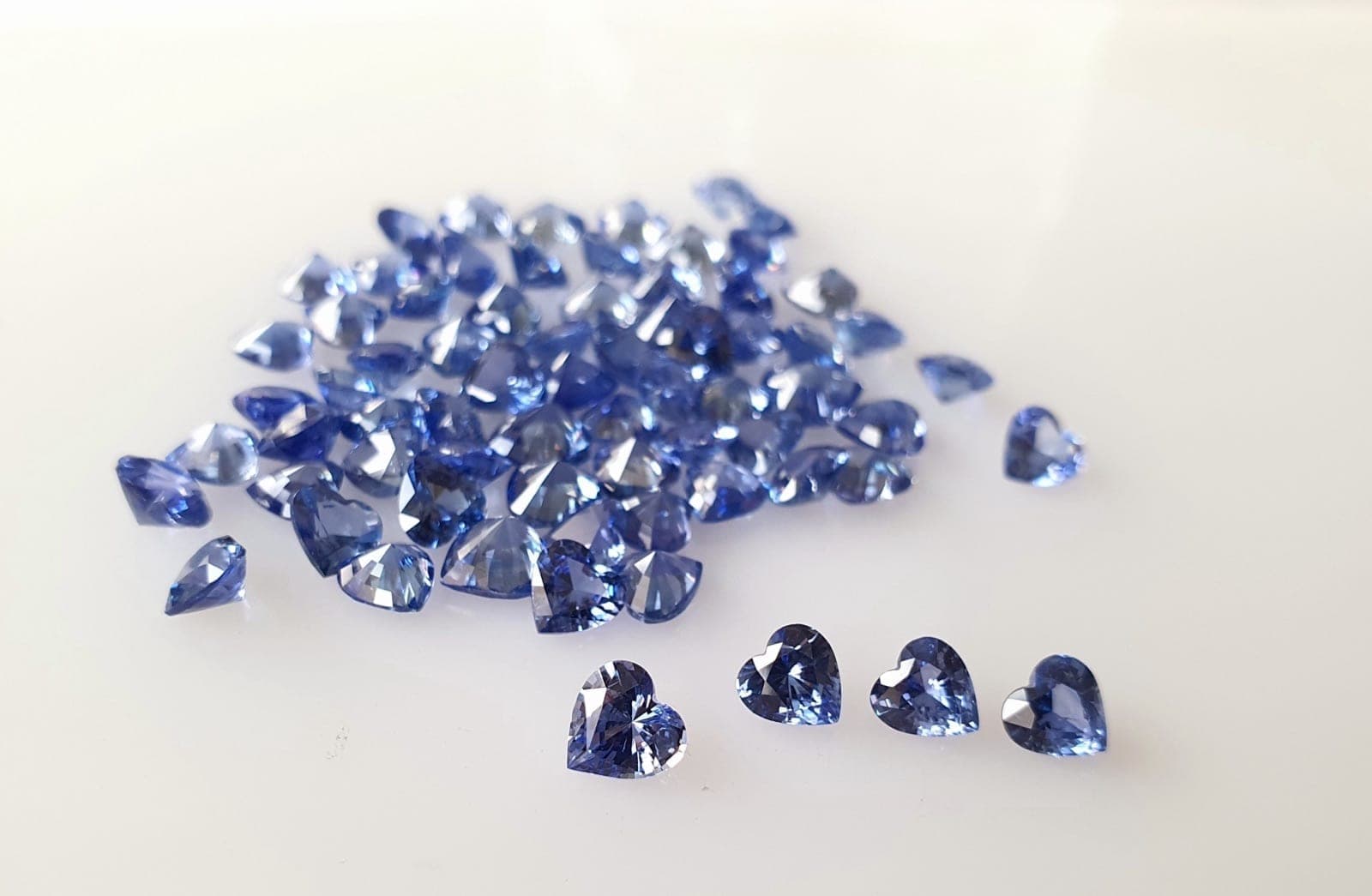 Ceylon sapphire (left, bright cornflower blue) beside a Thai sapphire (right, deeper inky blue-green) side by side under D65 daylight lighting