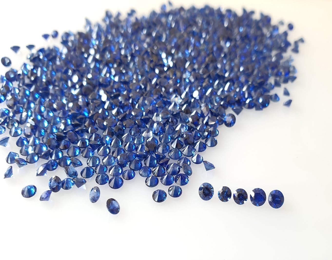 Mixed wholesale parcel of Ceylon and Thai sapphires sorted into origin-labeled trays on a dealer's sorting pad in Bangkok