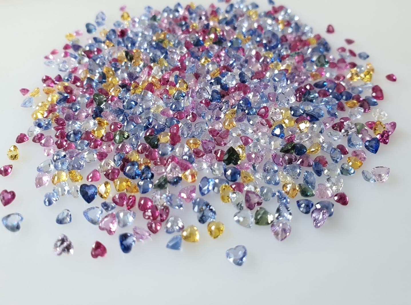 Jewelry designer reviewing gemstone samples — a spread of calibrated sapphires, rubies, and tourmalines on a design workbench beside jewelry sketches and a specification sheet