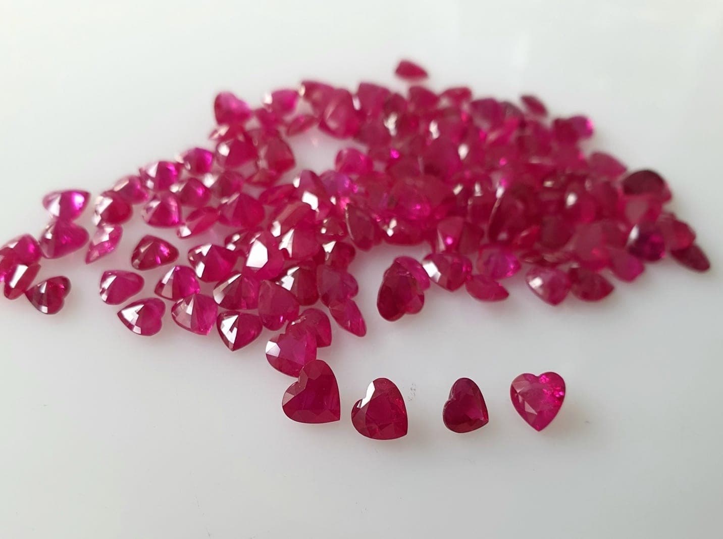 Gemologist at a Bangkok lab bench using UV light source to test ruby fluorescence response, with a natural Burmese ruby (strong red glow) and a flame-fusion synthetic (very strong red glow) side by side