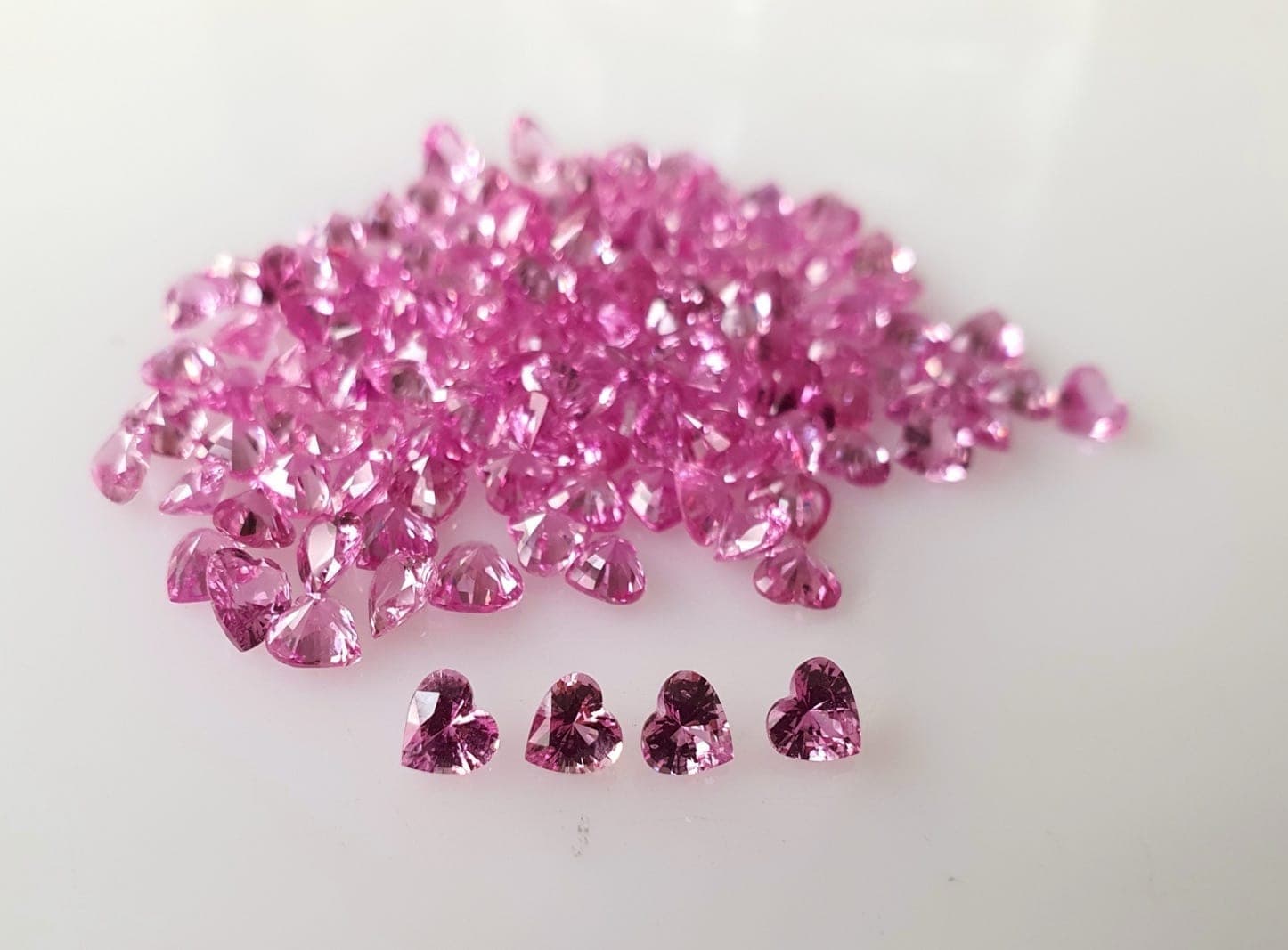 Curated padparadscha and pink sapphire inventory side by side in labeled compartment tray at a Bangkok wholesale desk, showing the full range from pale pink to vivid padparadscha salmon
