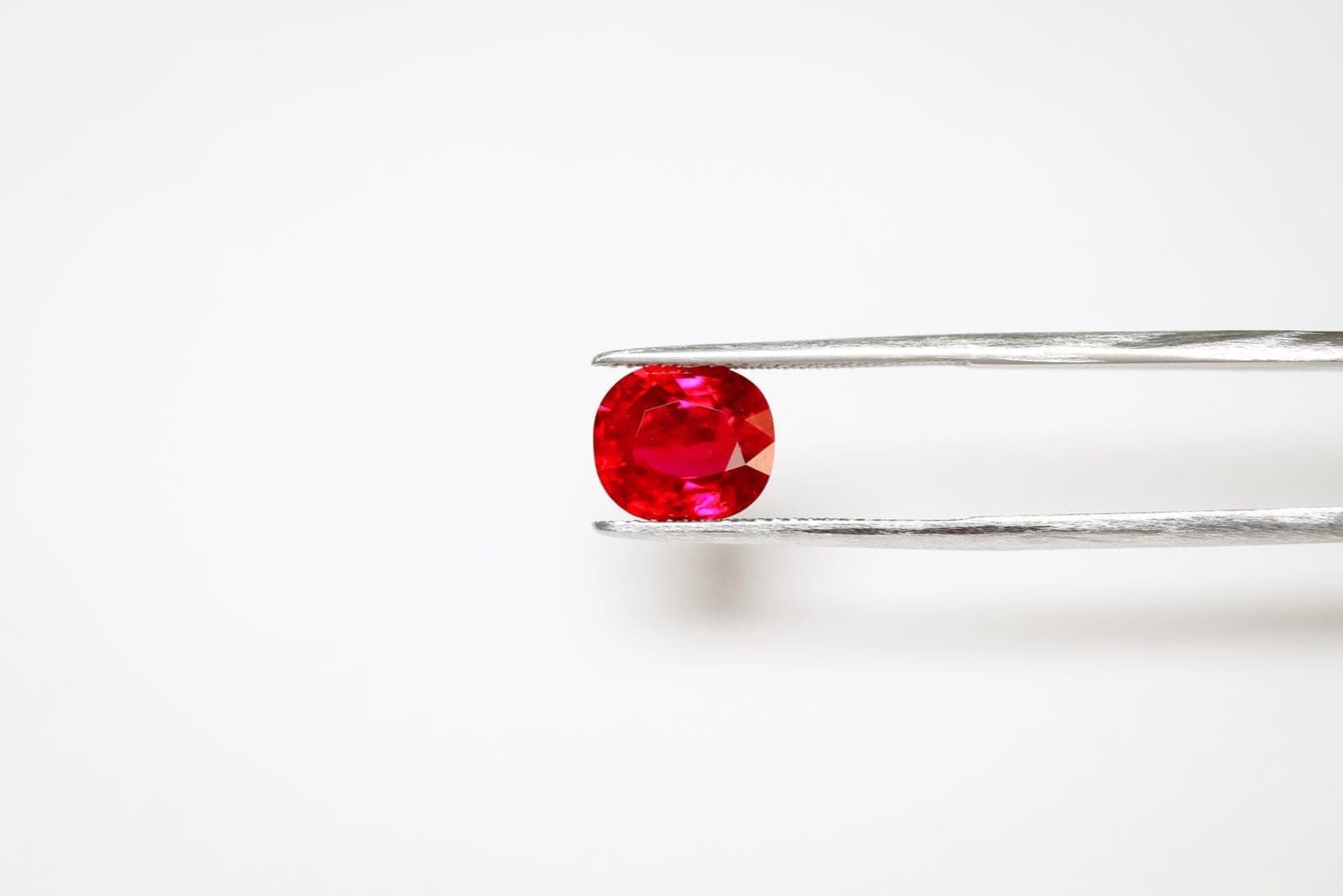 Five rubies arranged showing the color grade spectrum from pigeon blood vivid red through fine red, good red, commercial red, to low commercial — under D65 daylight lighting