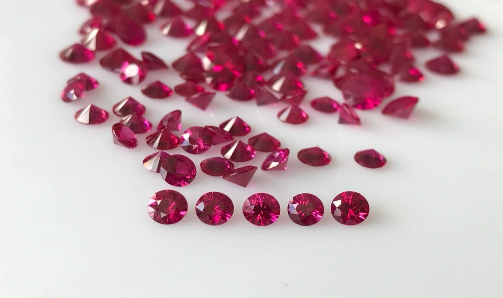 Rubies of different quality tiers arranged on a dealer sorting pad with price-per-carat labels, from commercial melee to exceptional pigeon blood stones