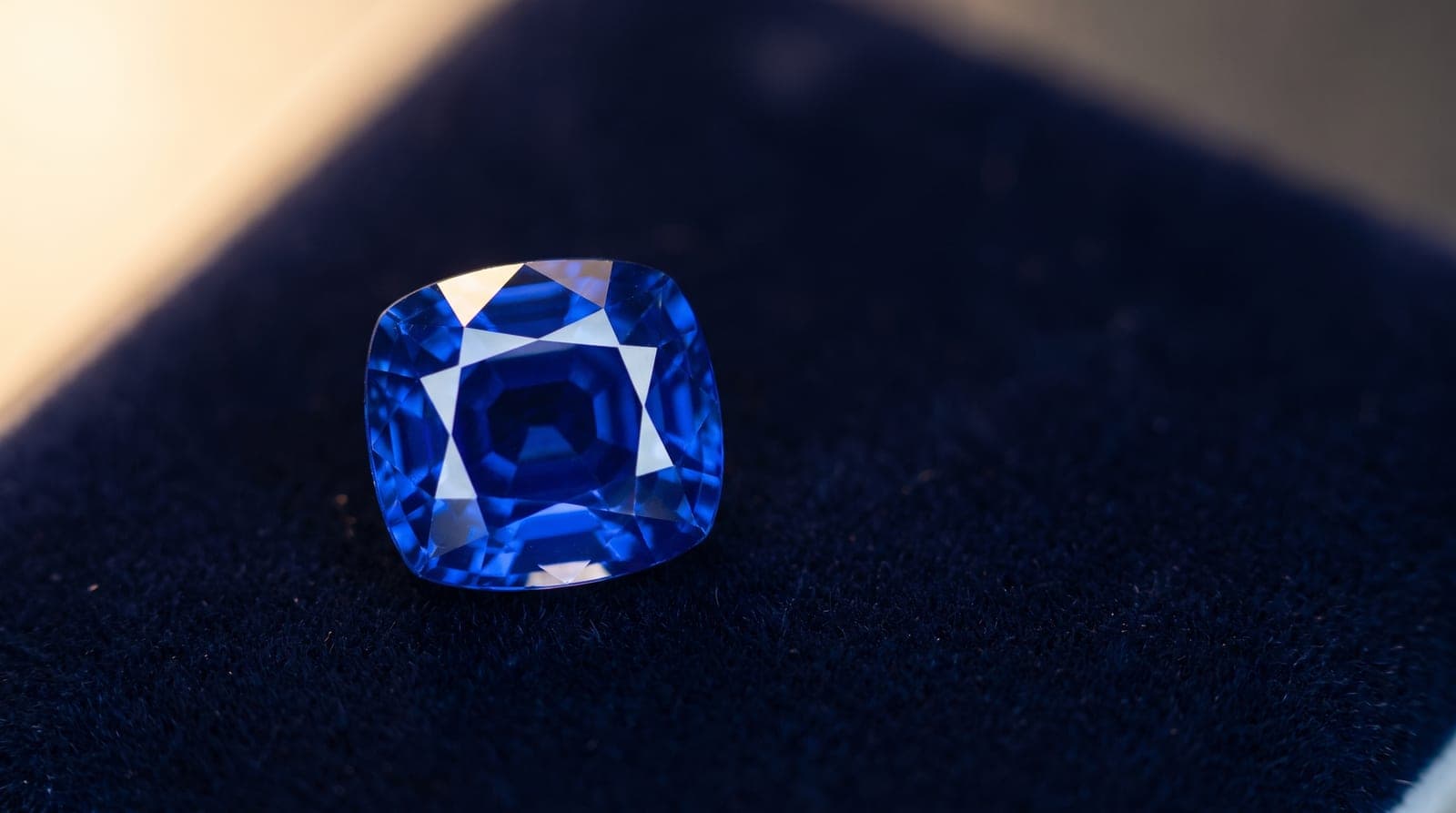 A clean, glowing royal-blue unheated cushion sapphire on dark velvet