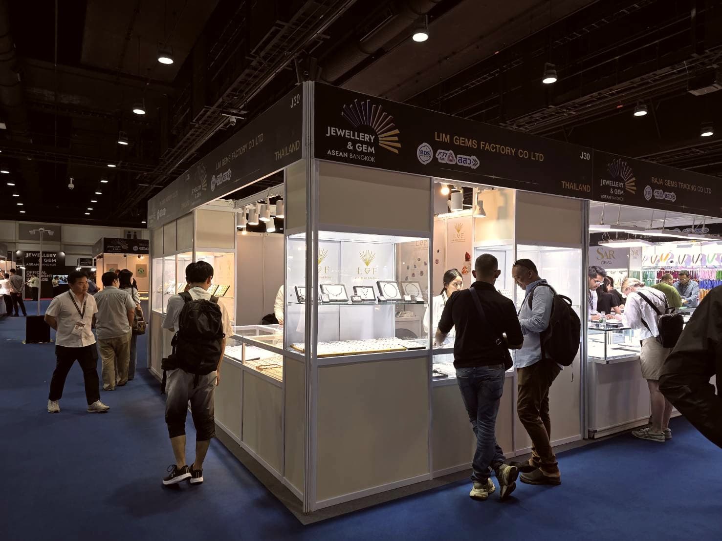 Lim Gems Factory booth at the Jewellery and Gem ASEAN trade fair in Bangkok, with international buyers reviewing sapphire and ruby parcels