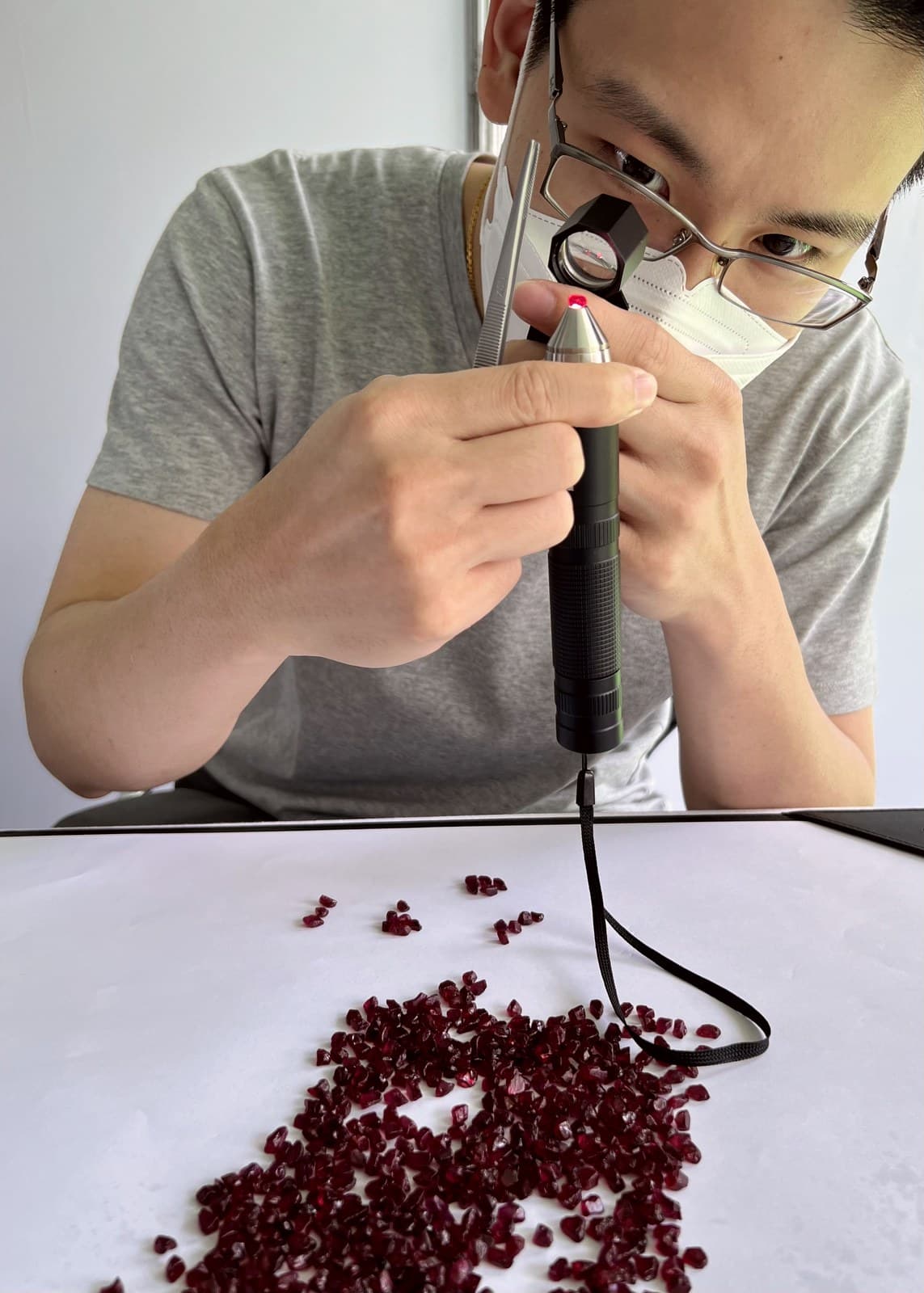 A Lim Gems Factory cutter inspecting a parcel of rough rubies with a loupe and torchlight before sorting